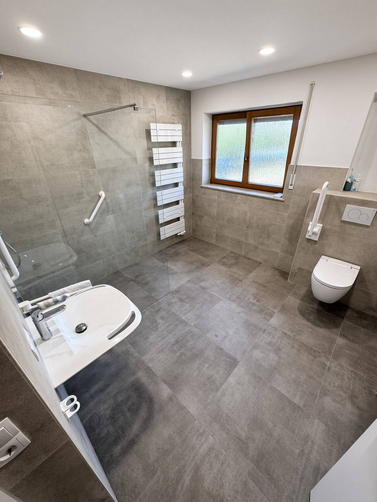 Modern saniertes Badezimmer mit grauen Wand- und Bodenfliesen